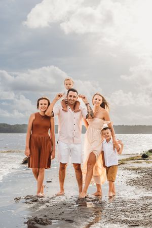 Family of five walks barefoot along a tropical beach shoreline under a cloudy sky. Jacksonville, NC