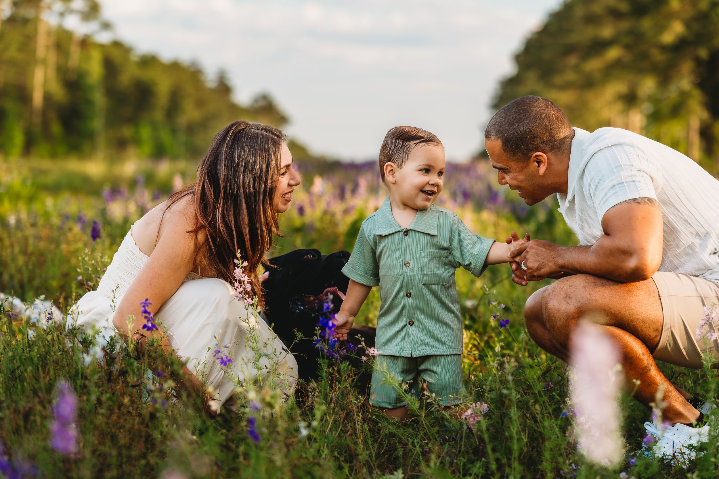 Family of three sharing a joyful moment in a wildflower field, with parents smiling at their toddler son.