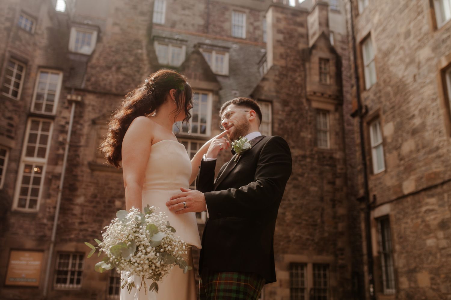 A romantic wedding moment captured against historic stone architecture with delicate baby's breath bouquet.