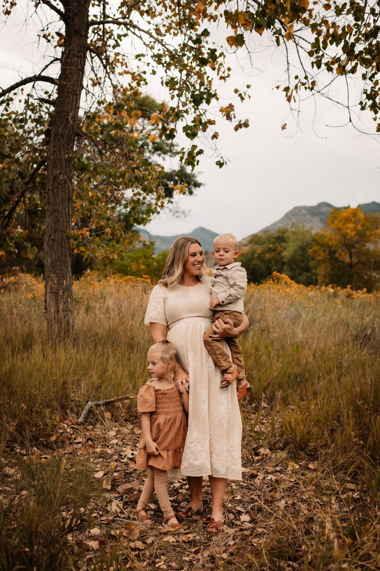 Fall family portrait in a rustic field with mountains and autumn foliage in the background.