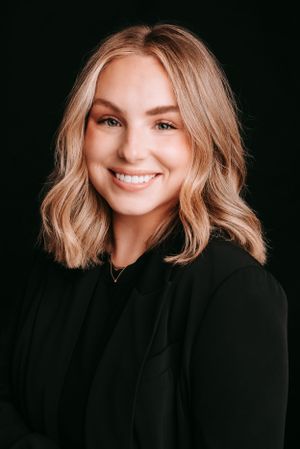 Professional headshot of woman in black top against dark background.