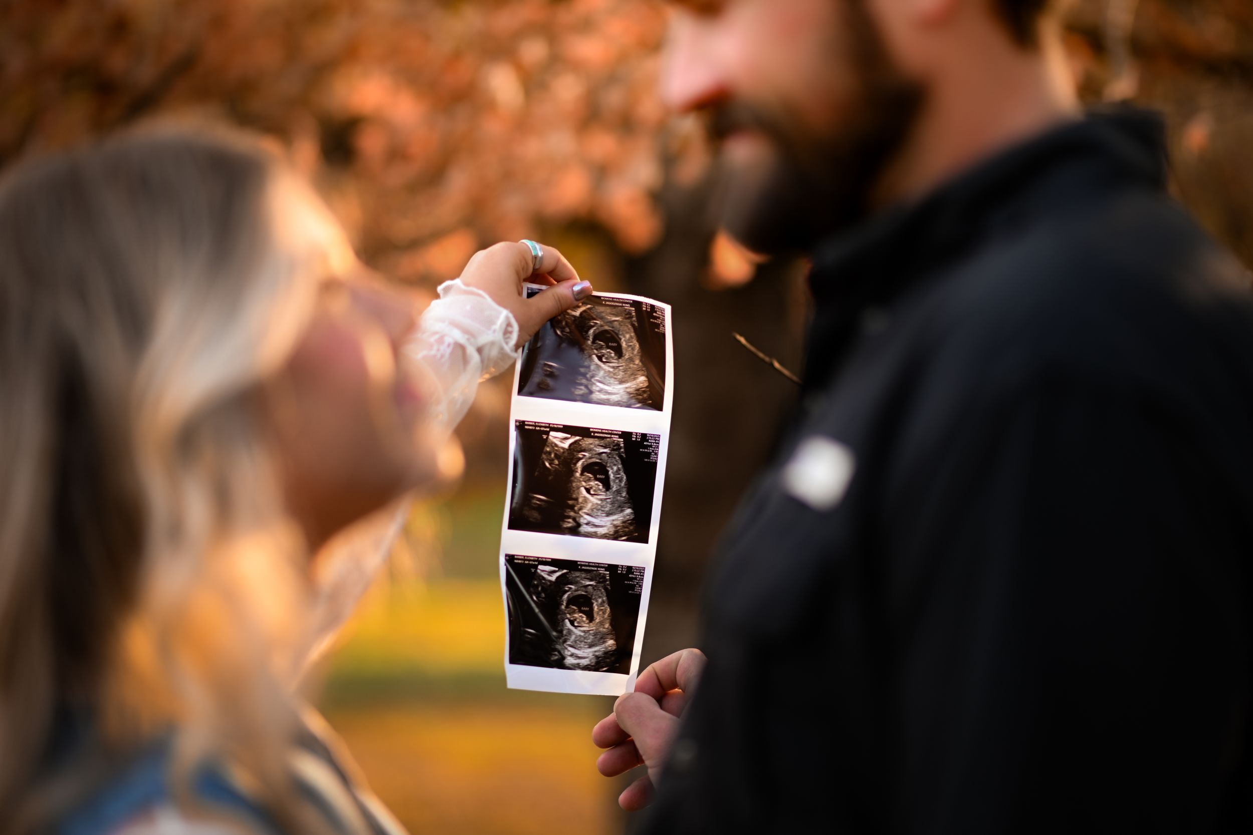A couple holds ultrasound photos during an outdoor pregnancy announcement photoshoot.