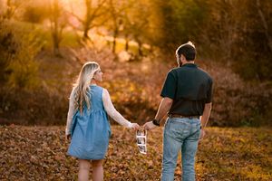 A couple walks hand in hand through a golden autumn field at sunset creating a romantic silhouette.