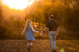 Two people stroll together in a warm sunset glow across an autumn landscape.
