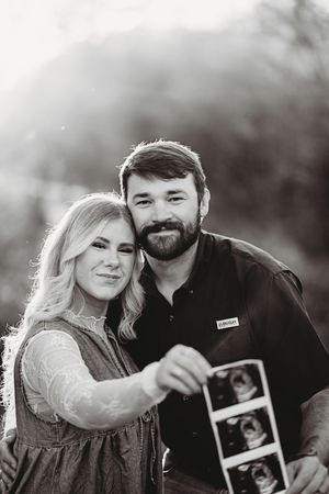 Couple sharing joyful moments while holding an ultrasound photo in an outdoor setting.