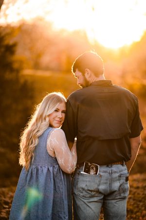 Couple walking together during golden hour with sun flare and autumn scenery.