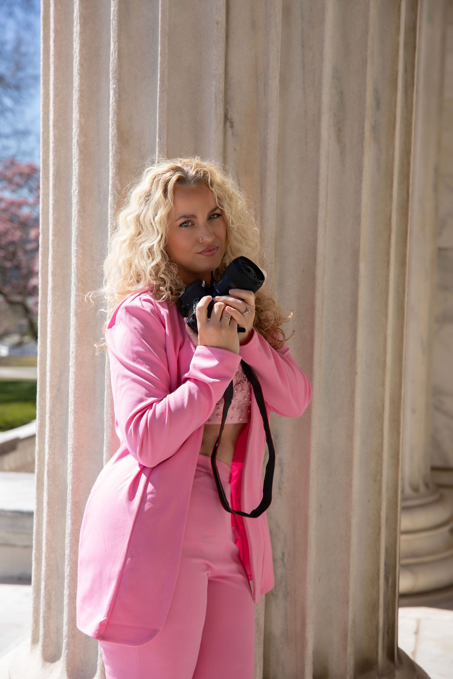 Professional photographer in pink blazer takes photos between classical white columns in architectural setting in Cleveland Ohio.
