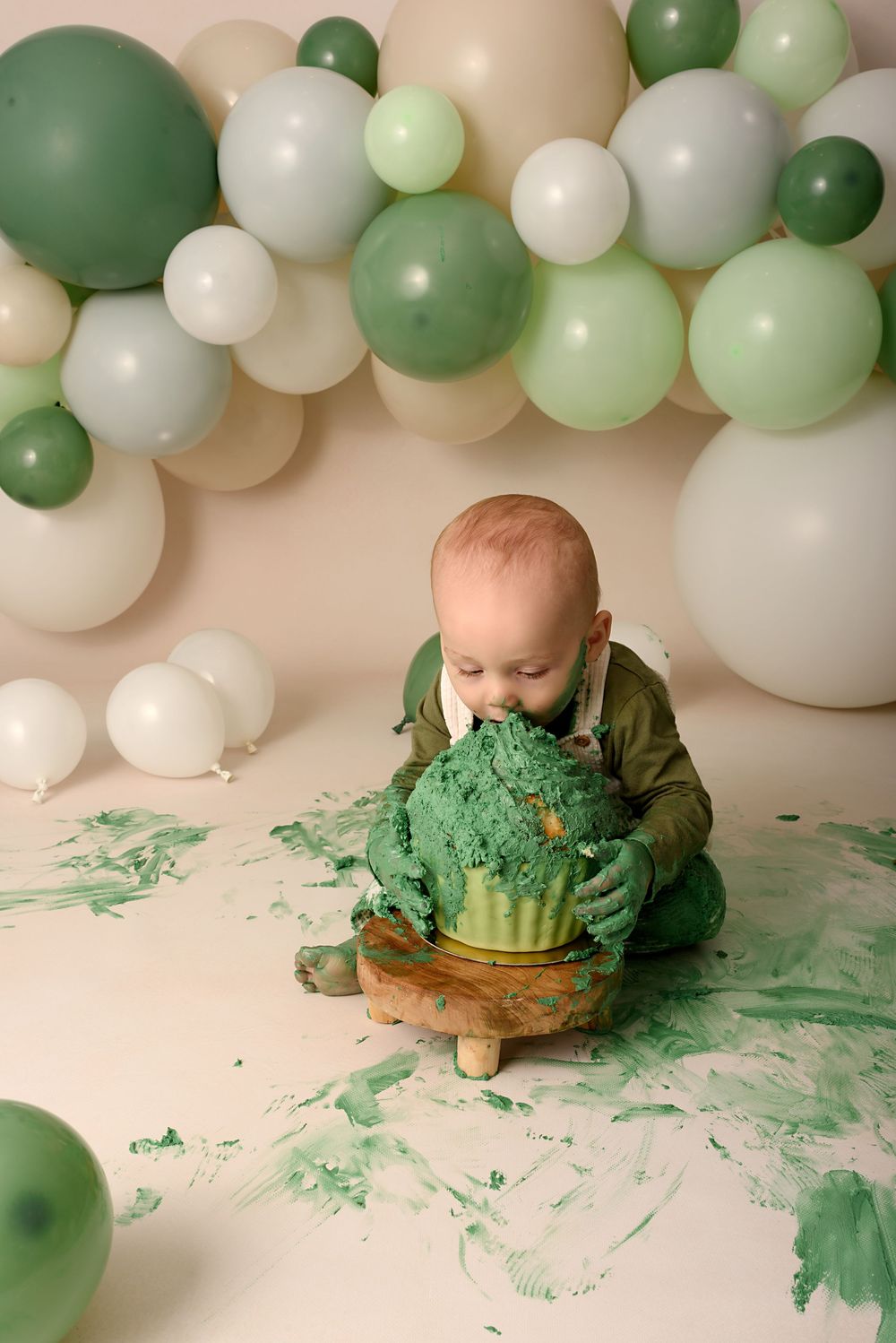 Green themed cake smash photography session with balloon arch and messy frosting.