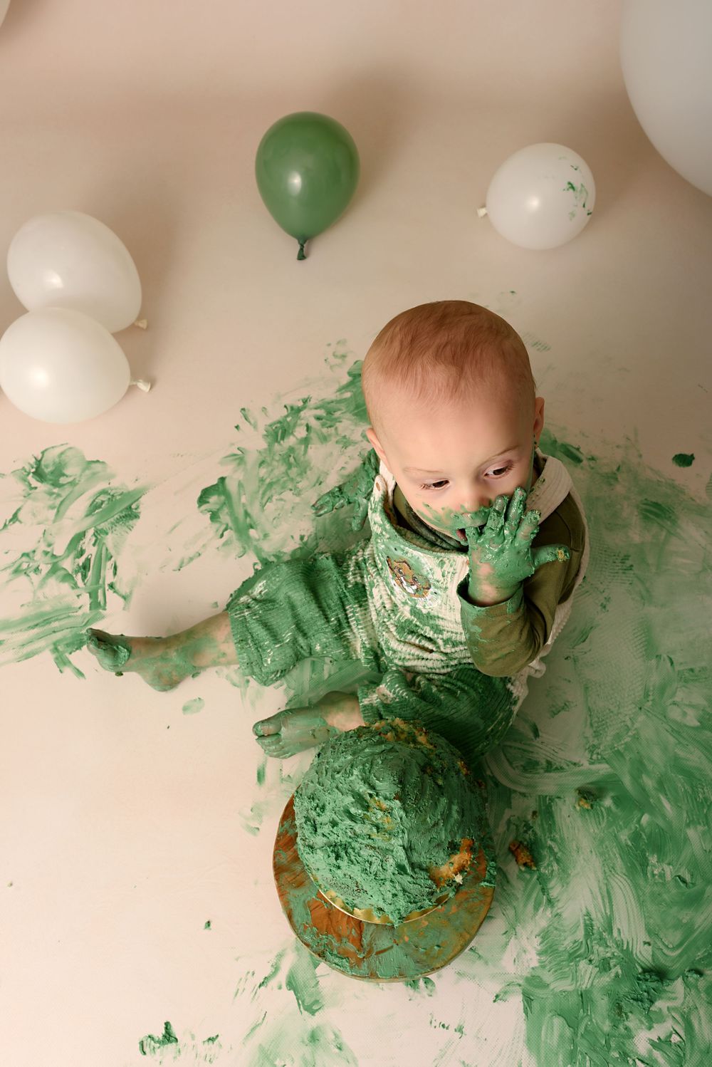 Messy cake smash photography session with green frosting spread across white backdrop.