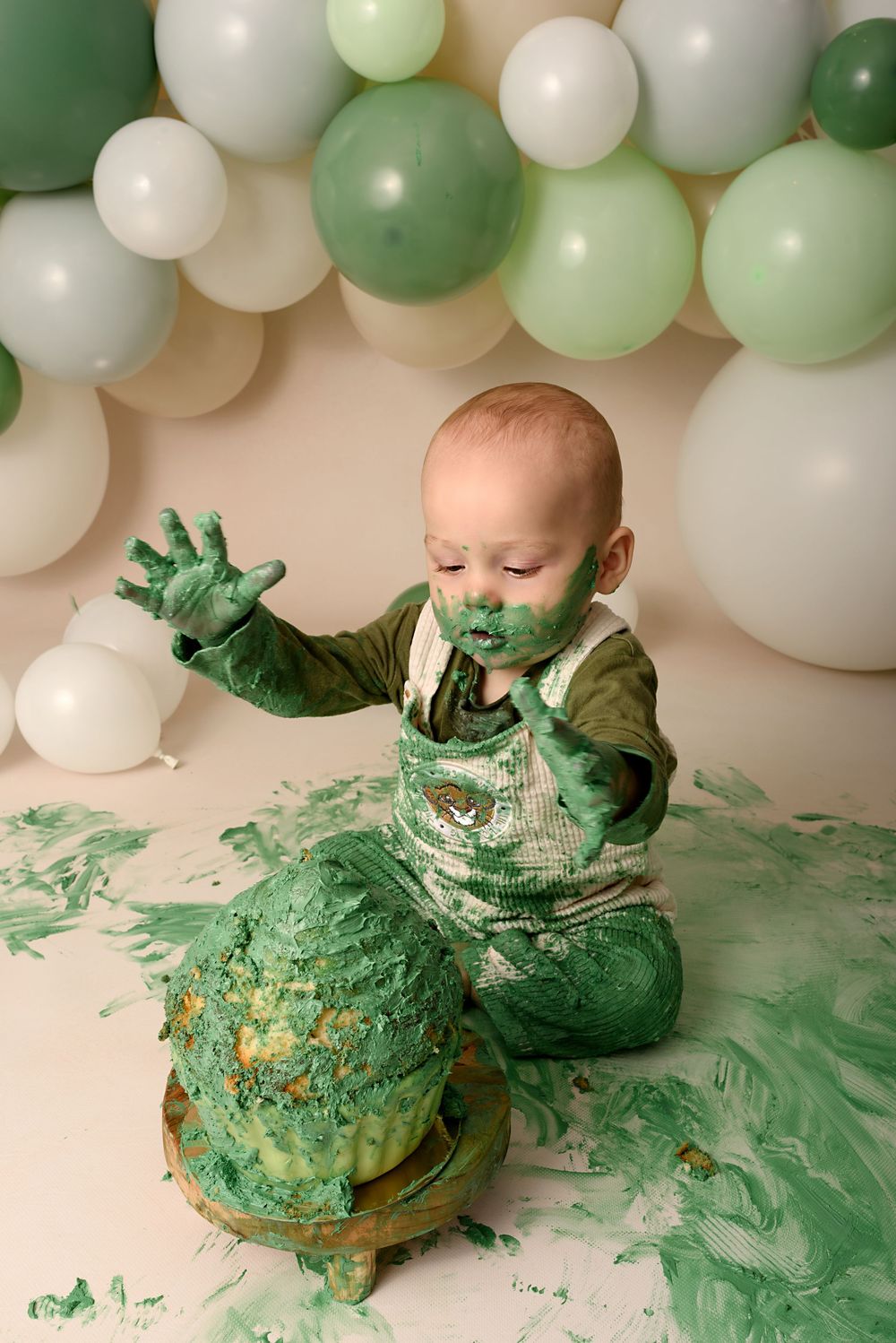 First birthday cake smash with green frosting and balloon garland decoration.