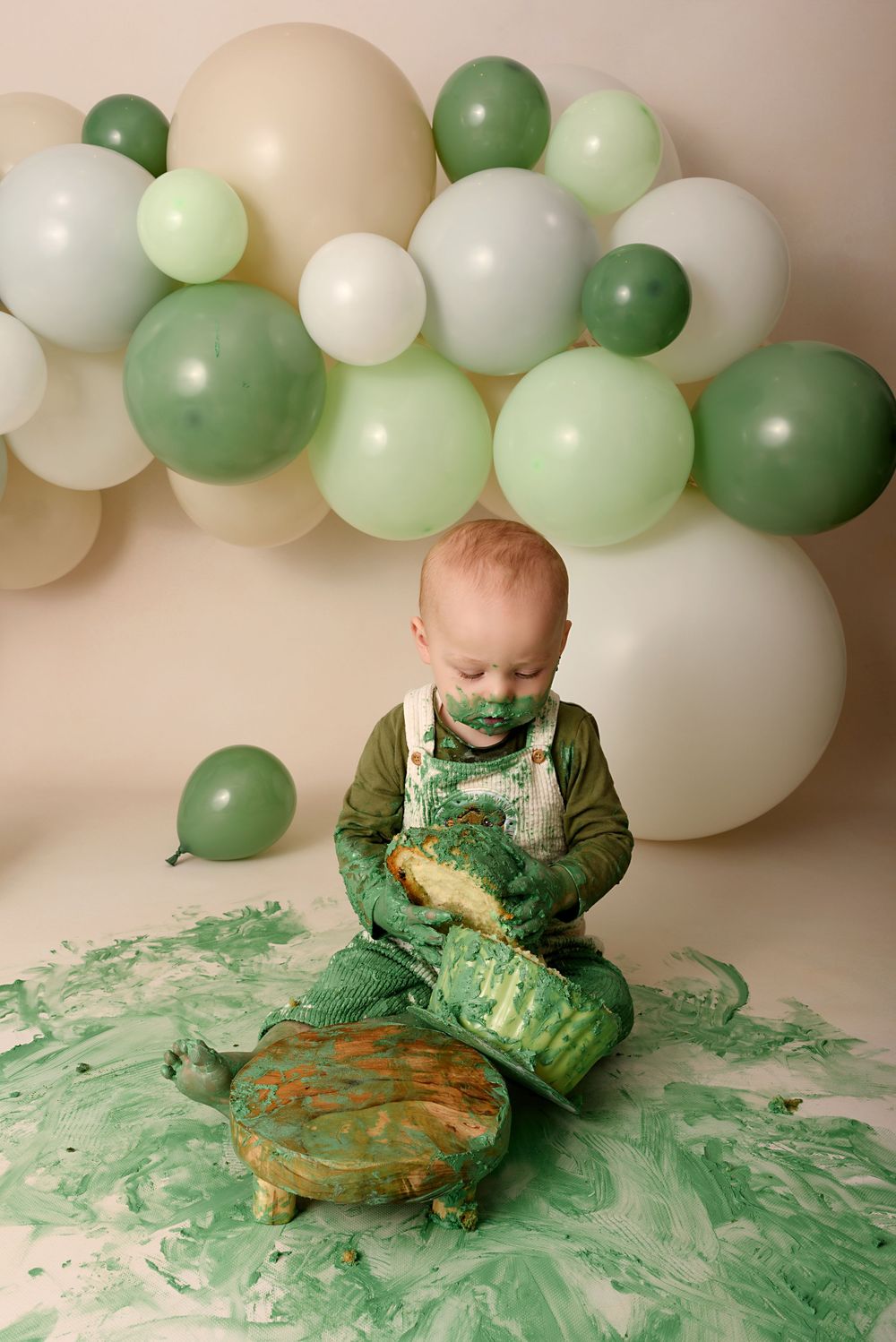 Cake smash photo sequence showing green frosting getting messier with white and green balloon backdrop.