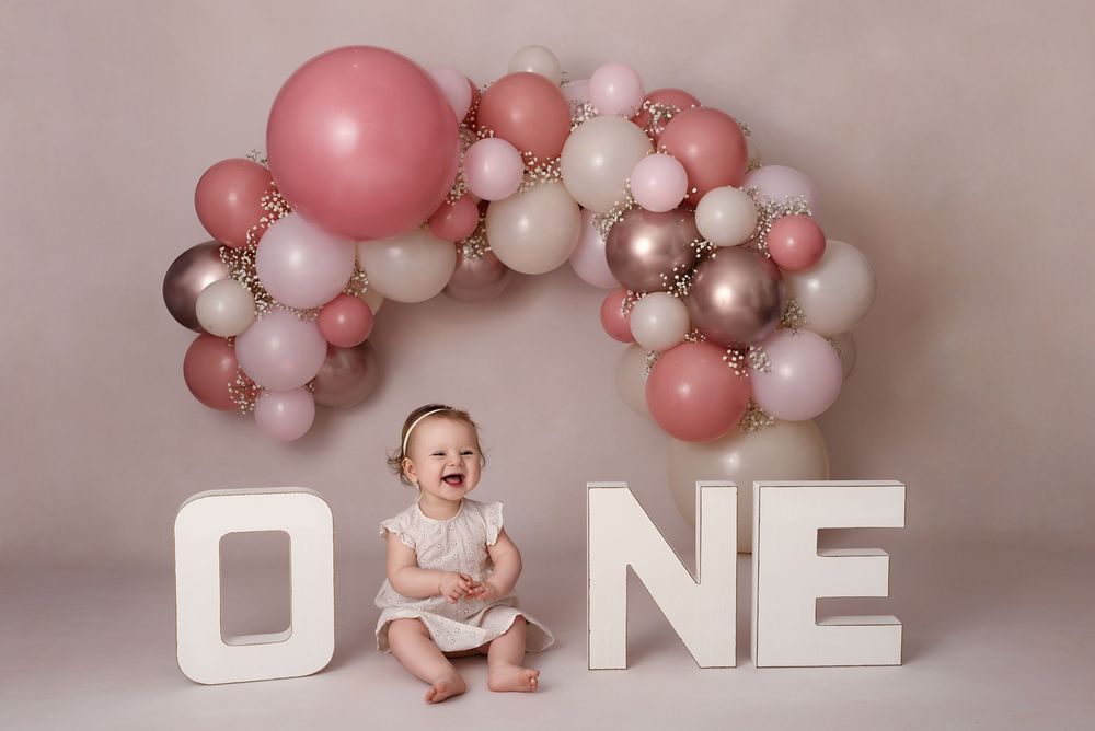 Baby sitting between white ONE letters under pink and beige balloon arch.