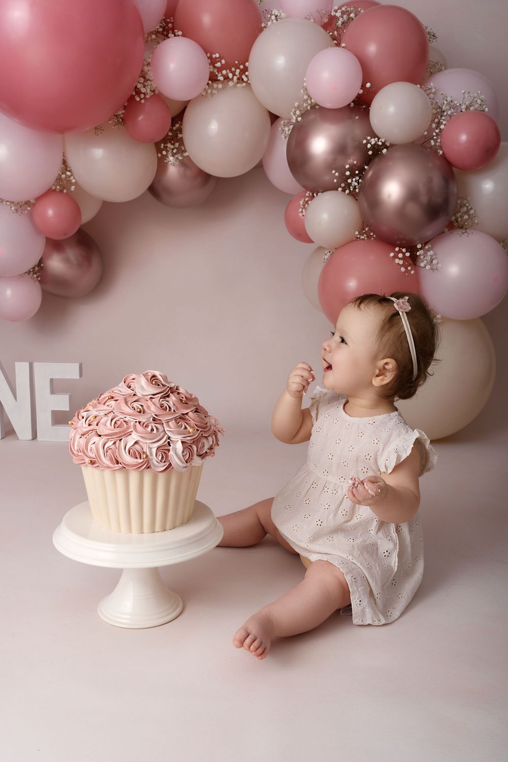 Pink and white balloon arch decorates a first birthday cake smash photo session with delicate styling.