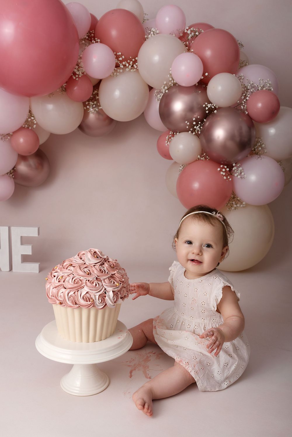 Elegant cake smash session featuring pink frosted cake and balloon arch in rose gold tones.