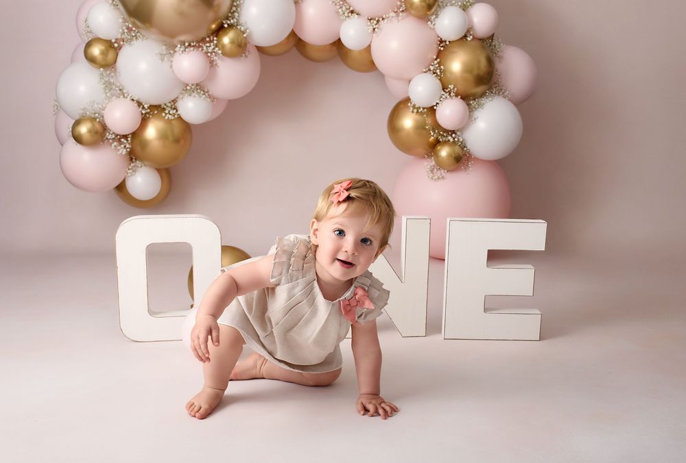 Birthday setup with gold and pink balloon arch and white block letters.