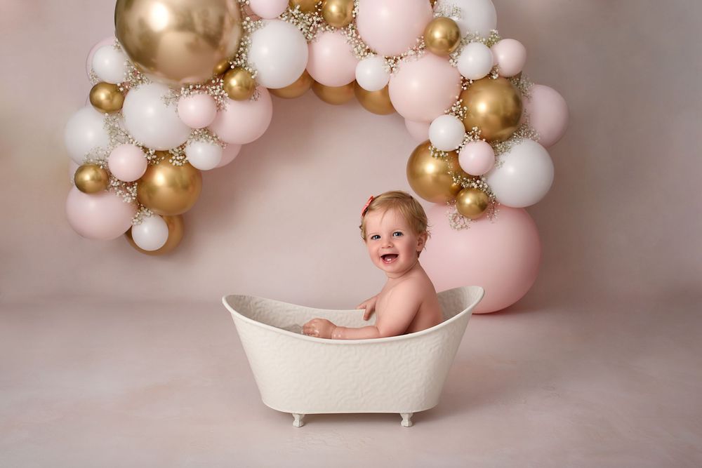 Bathtub prop surrounded by elegant pink and gold balloon garland for birthday photos.
