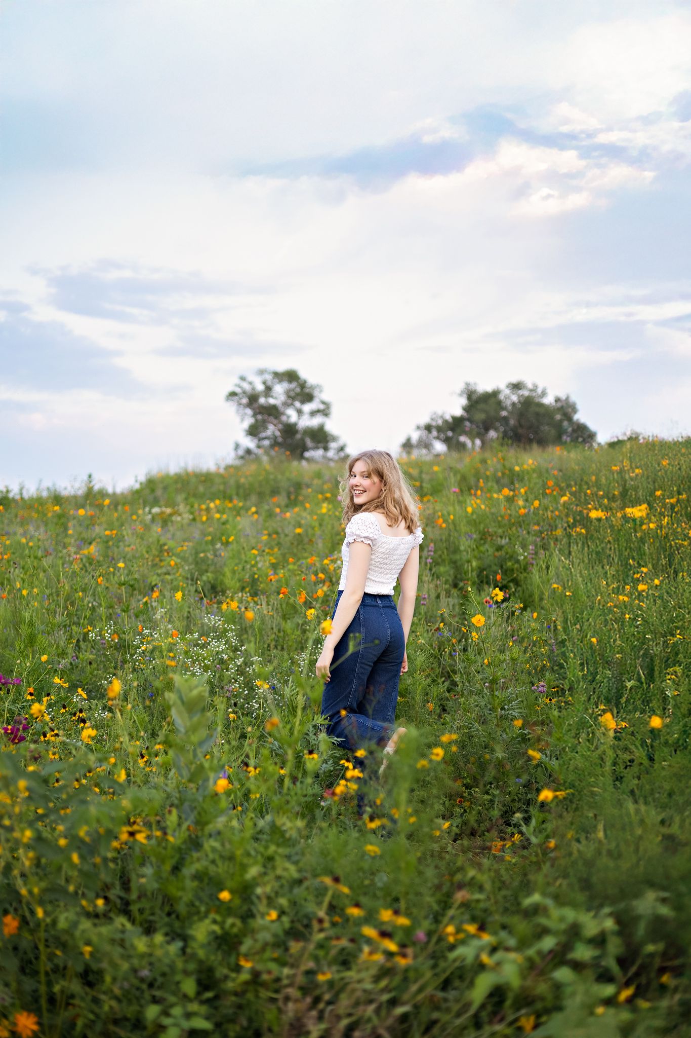 A person in a navy and white dress stands in a vibrant wildflower meadow filled with yellow and orange blooms.