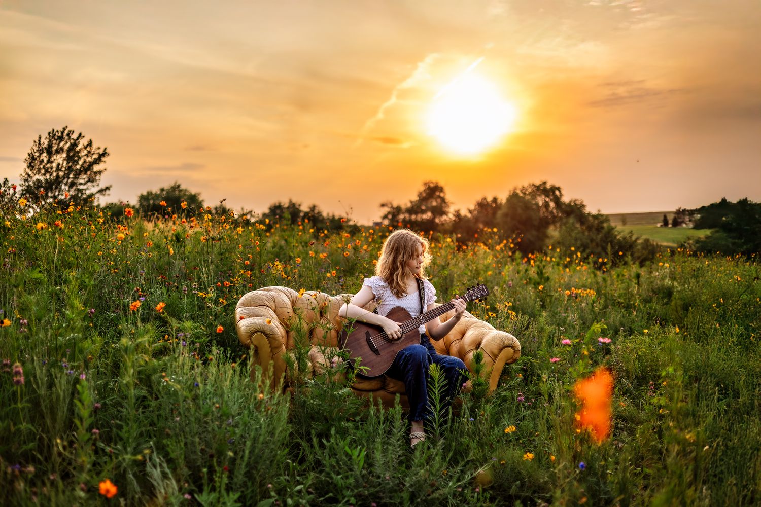 A person plays guitar in a wildflower meadow at sunset with two golden retrievers by their side.