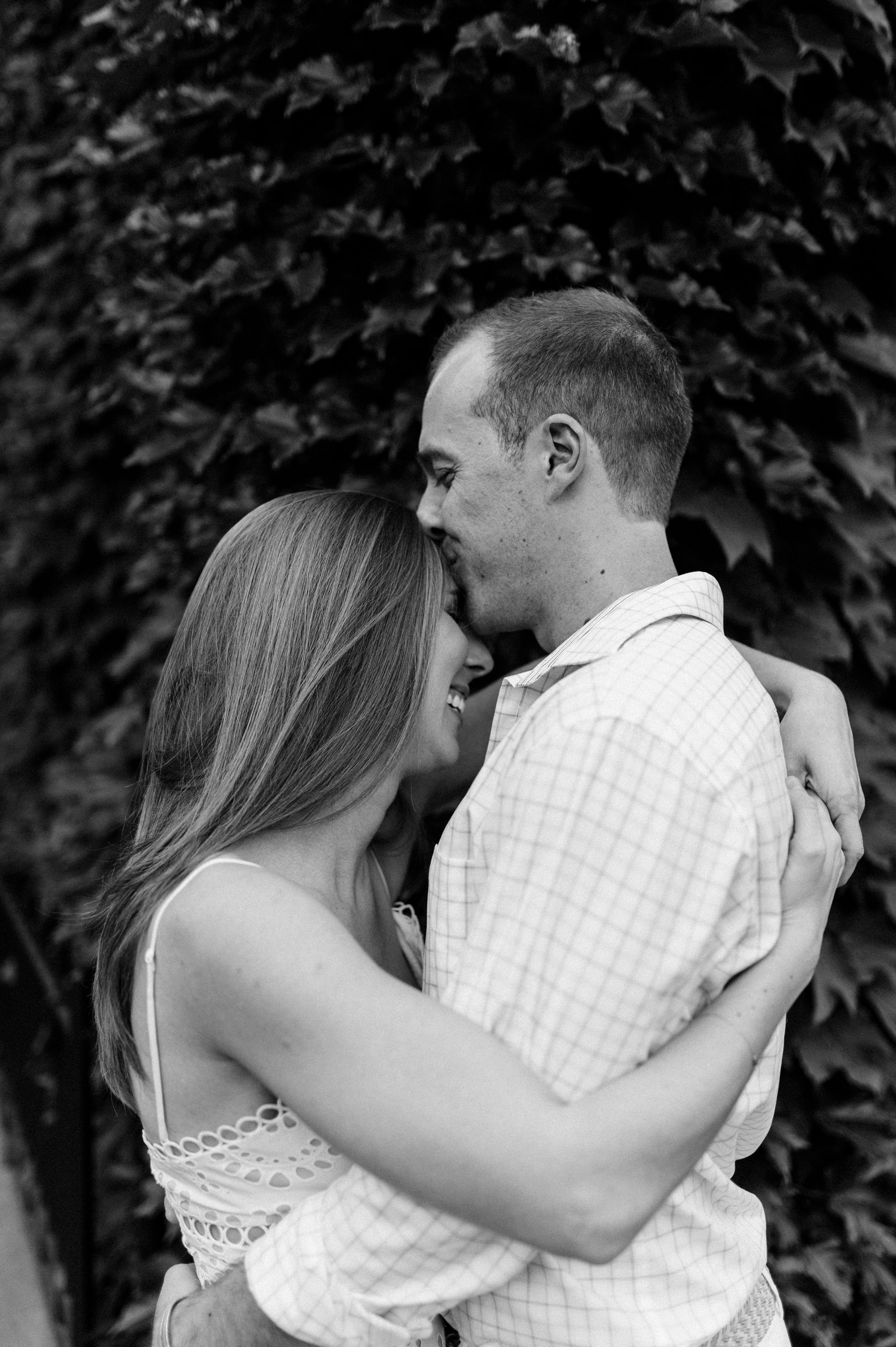 A romantic black and white portrait of a couple embracing in front of an ivy-covered wall.