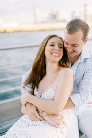 Happy couple embraces by the waterfront during golden hour engagement photoshoot.