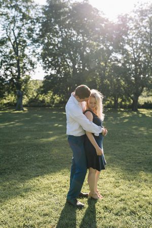Couple embraces in sunlit garden setting with lush green trees in the background.