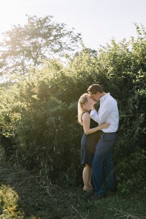 A romantic couple shares a tender embrace in golden sunlight against lush green foliage on a summer evening.
