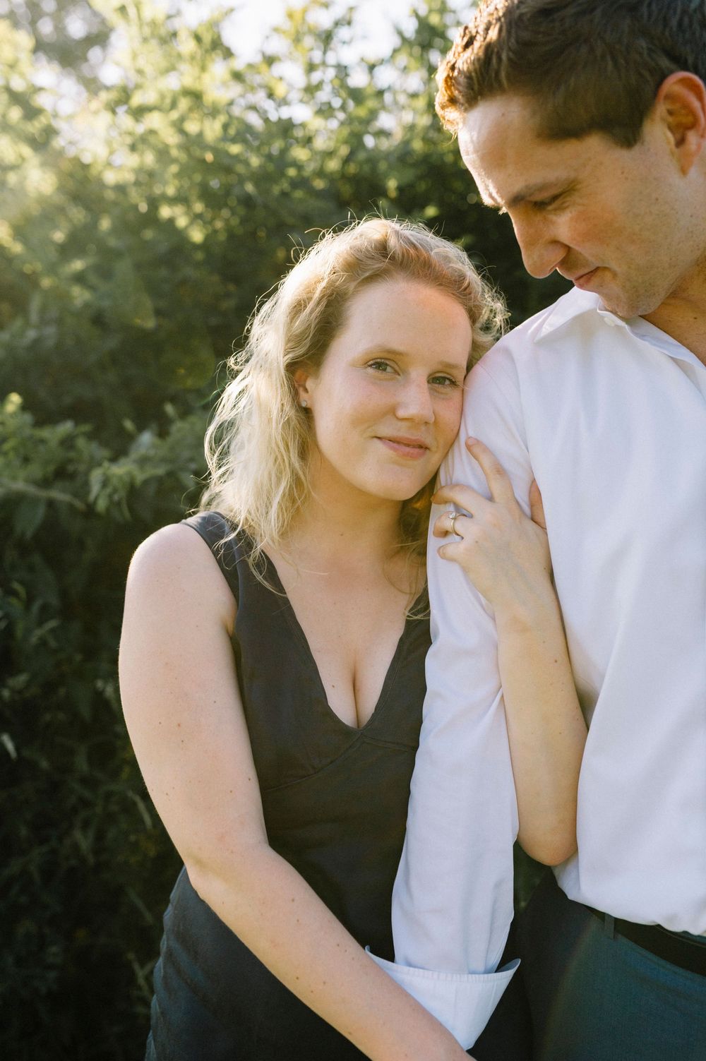 A romantic couple shares an intimate moment outdoors during golden hour against a sunlit background.