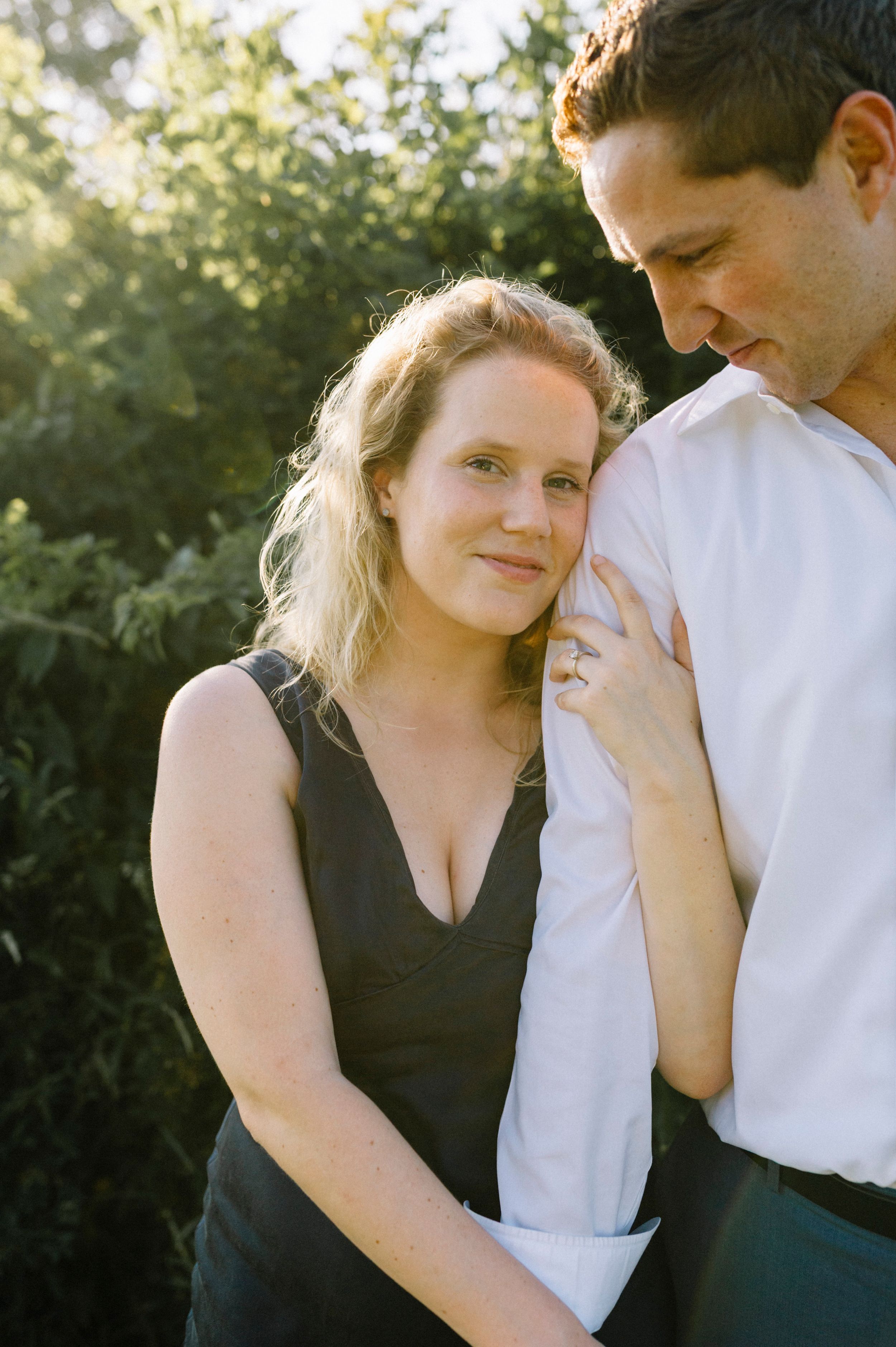 A romantic couple shares an intimate moment outdoors during golden hour against a sunlit background.