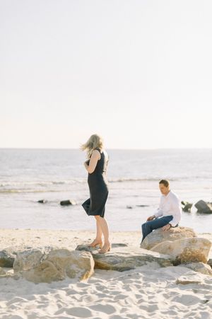 Two people enjoying a peaceful moment on rocky beach outcrops against an ocean backdrop at sunset.