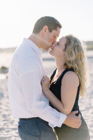 A romantic couple shares a tender moment while embracing on a sunlit sandy beach.