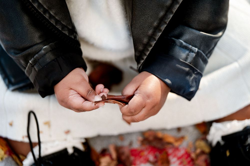 Close-up of hands holding a small brown wallet, wearing a black leather jacket over a white outfit.
