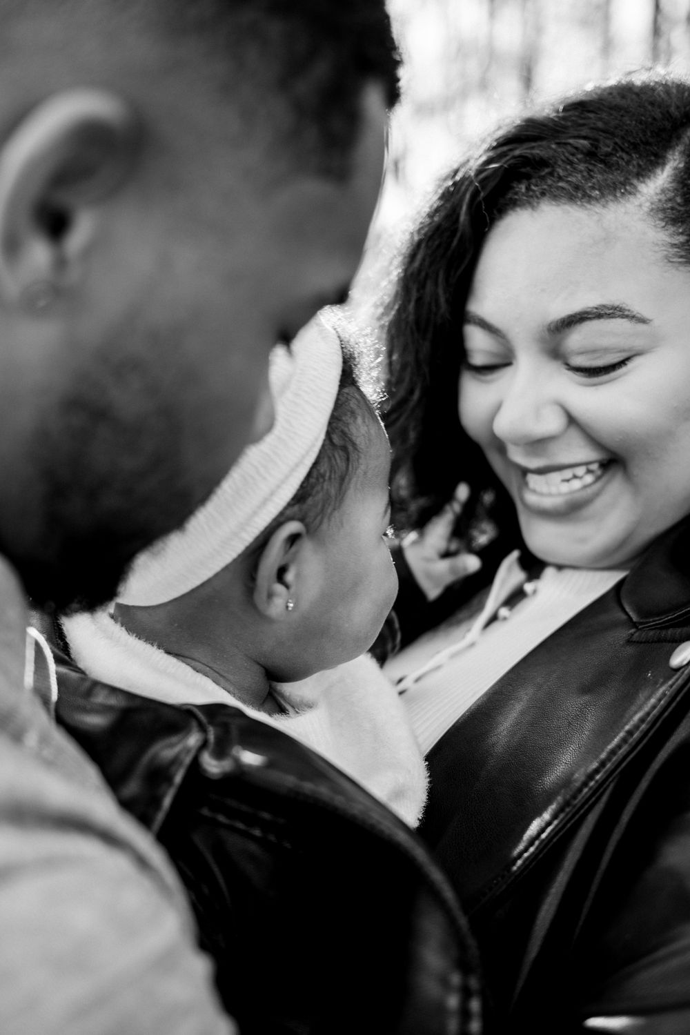 Black and white photo of smiling mother and father lovingly looking at their baby in an outdoor setting.