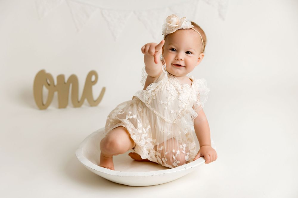 One year old baby girl sitting in a bowl with a ONE letters in the background