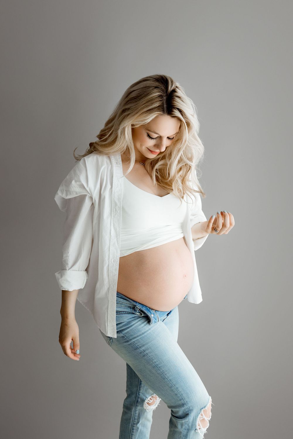 Simple Maternity Photoshoot on a gray backdrop. Mom is wearing jeans, white sports bra and white shirt.