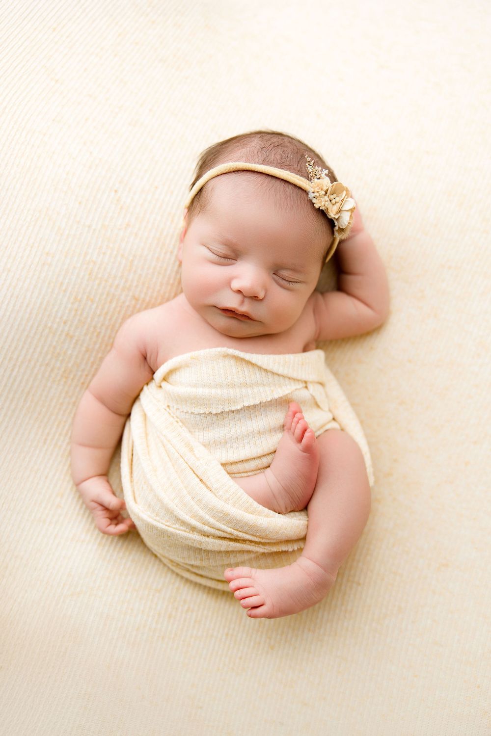 Newborn baby girl wrapped in light yellow wrap and flowery yellow headband, newborn photos