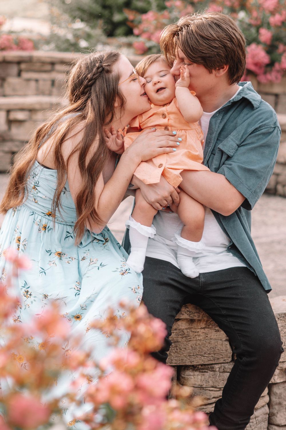 Family sharing playful moments together on a wooden bench surrounded by pink flowers.