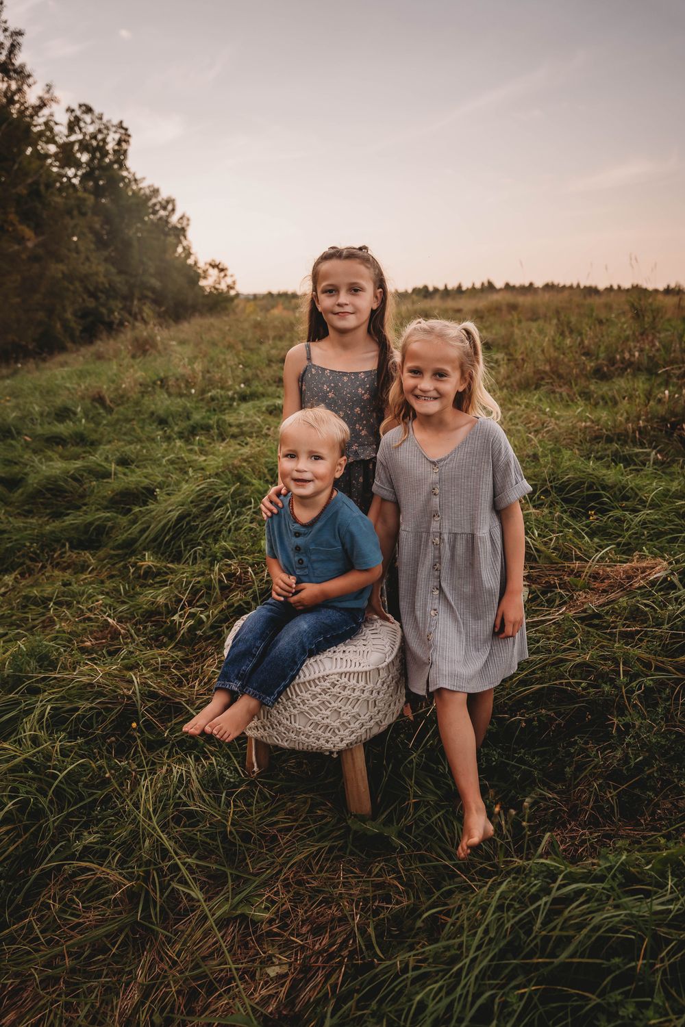 Children posing together in a grassy meadow at sunset with a woven basket.