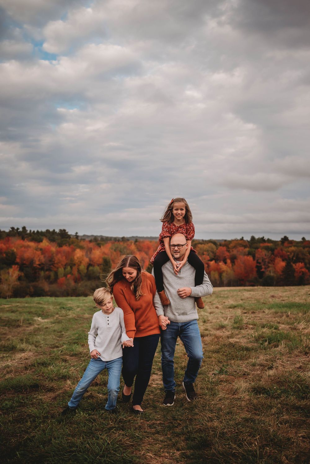 Group enjoying an autumn day on a hillside with vibrant fall foliage and cloudy skies in the background.