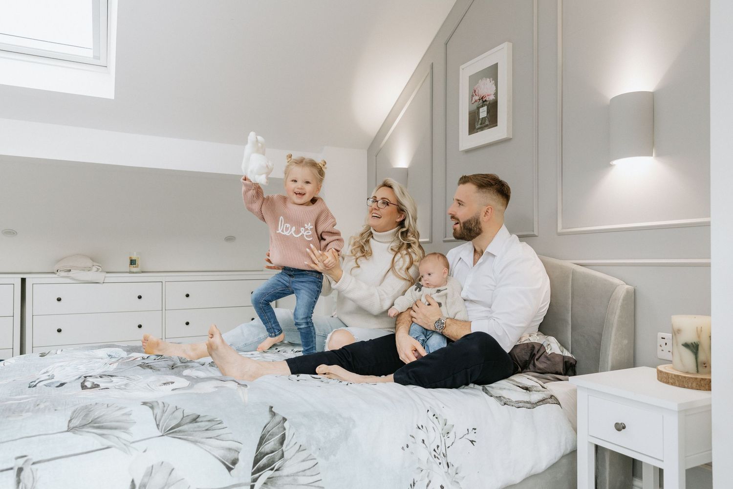 Family candid moments captured on white bed in bright modern bedroom.