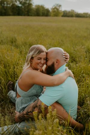 A couple shares an intimate moment while sitting in a sunlit summer field.