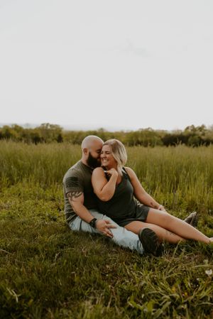 A couple lounges together in a grassy field during golden hour.