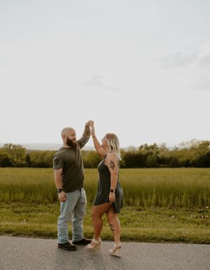A couple holding hands in a tender moment while standing on a path surrounded by grass and greenery.