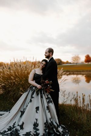 A dramatic white and black wedding dress photographed by a pond with autumn grasses.