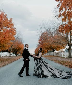 A dramatic wedding photo on a tree-lined autumn road with white fences.
