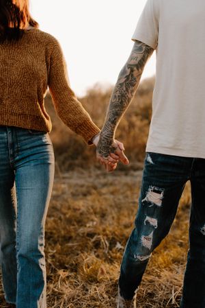 Close-up of tattooed arm holding hands at sunset with distressed denim details.