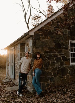 Casual couple leaning against stone building exterior at sunset with rustic aesthetics.