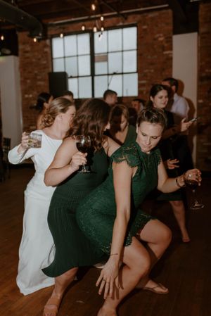 Wedding guests in formal attire dancing energetically at a reception in an industrial venue.