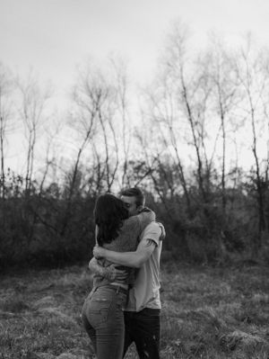 Black and white portrait of embrace against bare winter trees in natural setting.