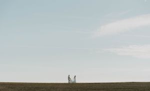 Two silhouettes stand together on a distant horizon against a clear sky.
