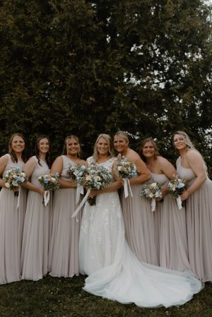 Wedding party wearing pale mauve bridesmaid dresses and white bridal gown pose together outdoors.